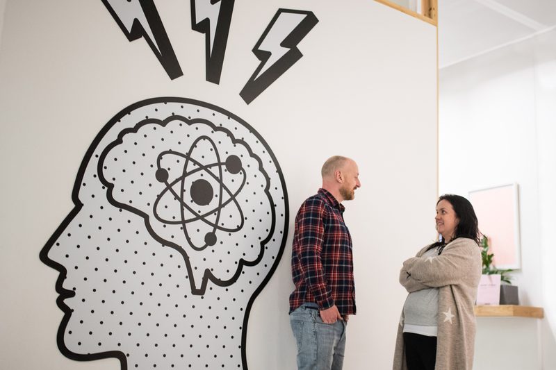 Two of the Chick team talking by a wall mural of a head with an atom for a brain